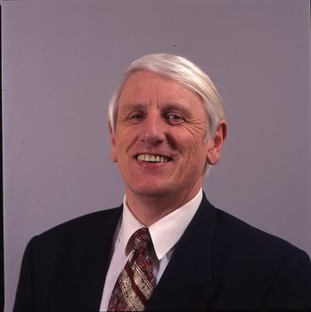 John Cook in dark suit with white shirt and red and gold tie