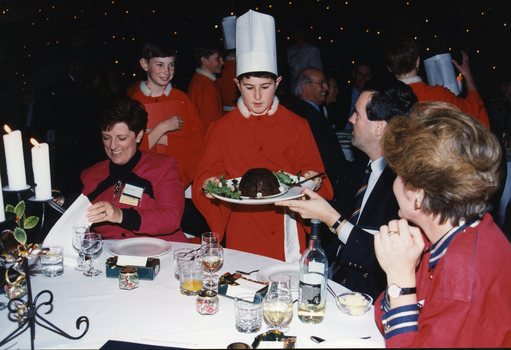 Chorister hands a Christmas pudding to a man with Carol O'Reilly on the left
