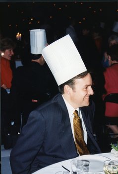 Profile of smiling man in a suit and wearing a paper chef's hat