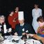 Man in centre wears a paper chef's hat, whilst the woman helps cut up the Christmas pudding
