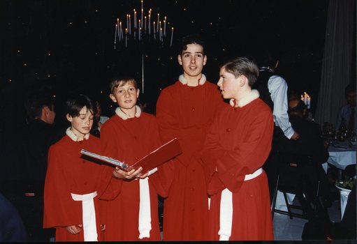 Four Choristers stand, one holding a song book
