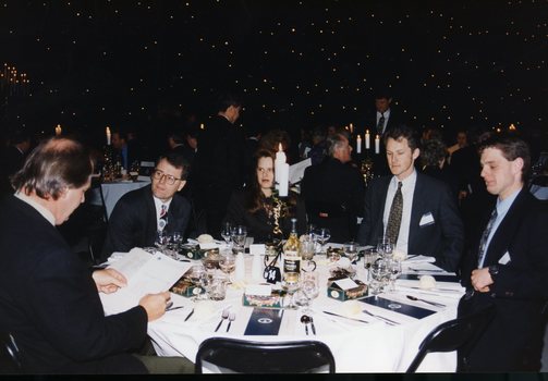 Five people around a table, with most looking past a man who is reading the menu