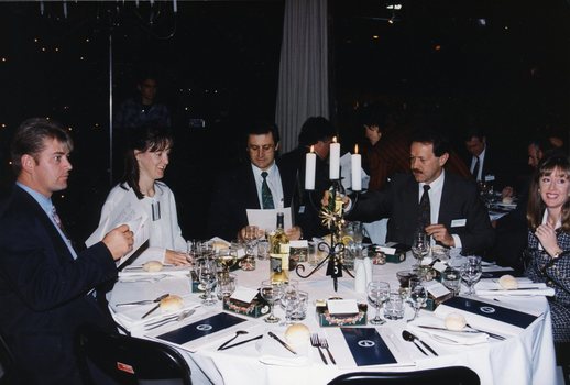 Three people around the table look at the menu, whilst two others pour wine or glance across the room