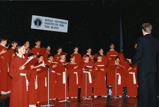 National Boys Choir dressed in red, with their conductor, in front of a starry backdrop and RVIB sign