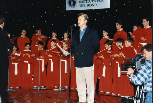 National Boys Choir dressed in red, with their conductor, in front of a starry backdrop with Peter Cupples