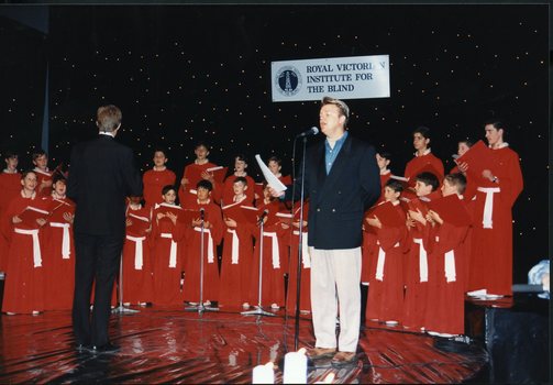 National Boys Choir dressed in red, with their conductor, in front of a starry backdrop with Peter Cupples
