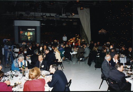 People seated around tables in Studio 1 at Channel 9 with a large television showing a male singer