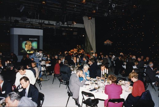 People seated around tables in Studio 1 at Channel 9 with a large television showing a male singer