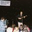 Peter Cupples on stage with guitar and a cameraman recording