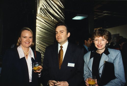 Two women and a man stand and smile for the camera with glasses in hand
