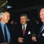 Three men stand and smile as they hold glasses of wine