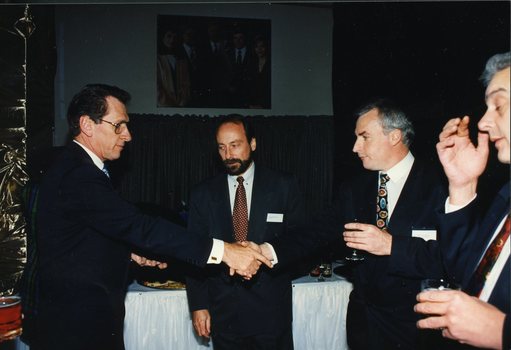 Two men shaking hands past a third man (Ross Johnstone)