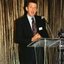 Acting CEO Len Evans gives a welcome address in front of a gold curtain