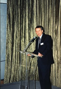Acting CEO Len Evans gives a welcome address in front of a gold curtain