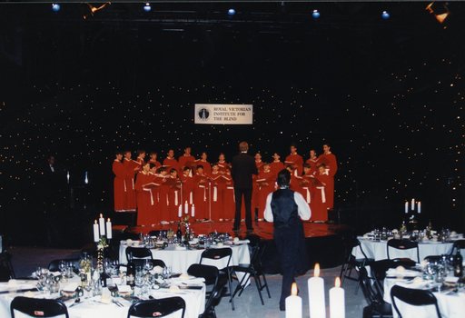 National Boys Choir dressed in red, with their conductor, in front of a starry backdrop with RVIB above them