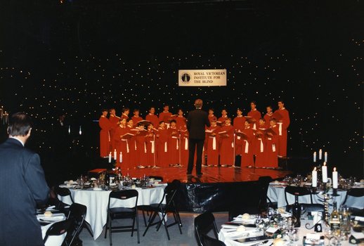 National Boys Choir dressed in red, with their conductor, in front of a starry backdrop with RVIB above them