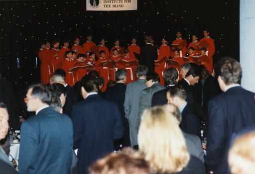 National Boys Choir dressed in red, with their conductor, and in the foreground guests stand around tables