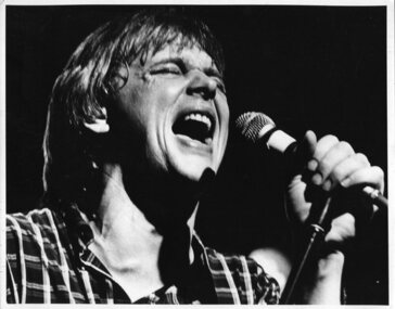 Man singing into microphone, wearing a checked shirt