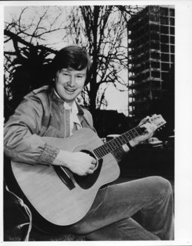 Man holding a guitar as he sits on a park bench in St Kilda Road