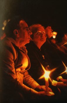 Two older people in the audience holding candles