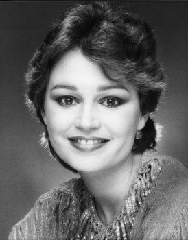 Black and white portrait of smiling woman with light shining behind her and on the sparkles on her jumper