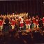 Children in red and white costumes dance on stage with Santa