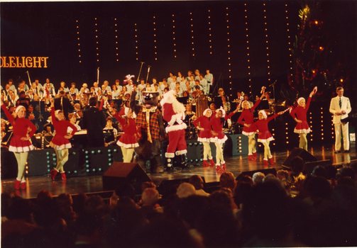 Children in red and white costumes dance on stage with Santa