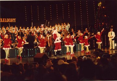 Children in red and white costumes dance on stage with Santa