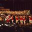 Children in red and white costumes dance on stage with Santa