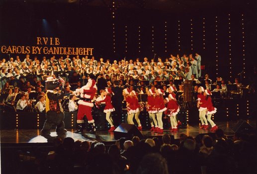 Children in red and white costumes dance on stage with Santa