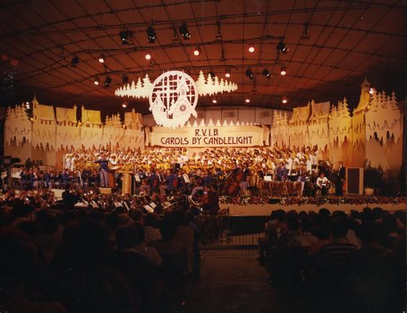 Outlines of white houses with snow and fir trees line the stage as the choir sings