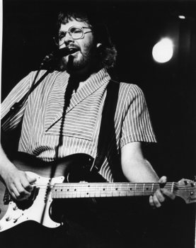 Man singing into a microphone as he plays guitar