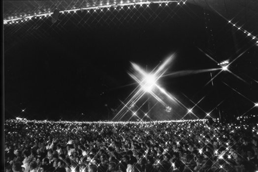 View from side of the stage as crowds hold their candles