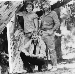 Three men stand or squat by a tree, whilst another is blocked out