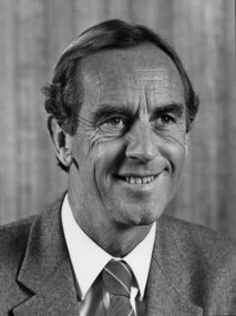 Man smiles to right of camera, dressed in jacket and tie