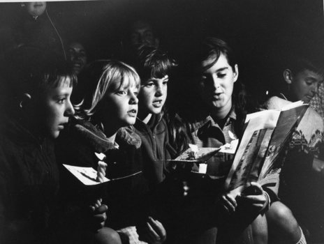 Four school children sit holding candles and singing from song books