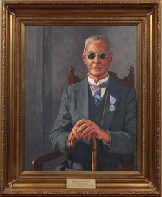 Man wearing dark glasses sits on a chair holding a cane