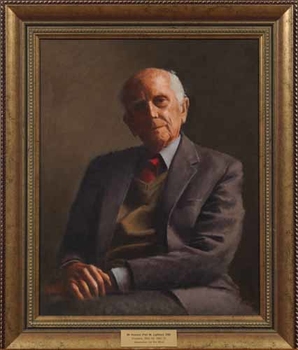 Elderly man in grey suit with green vest and red tie, with hands together on his lap to one side and tilted head looking outwards