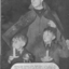 Serviceman uses his coat to keep rain off two boys with candles