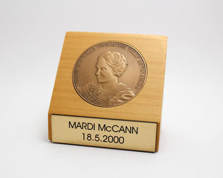 1 blonde wooden stand with gold tone inlaid medallion and nameplate on front 'Mardi McCann 18.5.200'