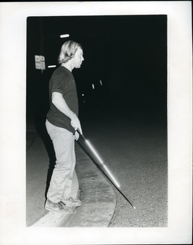Man standing on a kerb, using his white cane at night to cross the road