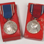 2 silver medals hanging from a red or blue ribbon with blue or red and white edging on top of red medal boxes