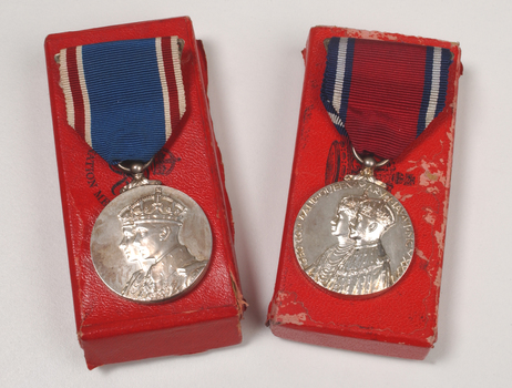 2 silver medals hanging from a red or blue ribbon with blue or red and white edging on top of red medal boxes
