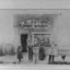 Four people stand outside of a shop with a sign E Aston Boot Maker