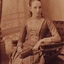 Tilly Aston as a young girl sitting in a chair with a handbag in her lap