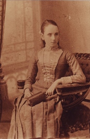Tilly Aston as a young girl sitting in a chair with a handbag in her lap