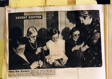 Four women sitting knitting whilst another lady stands as feels the knitting needles to ensure it is done right