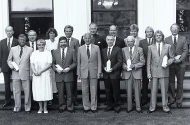 Group of people on steps of Government House holding awards