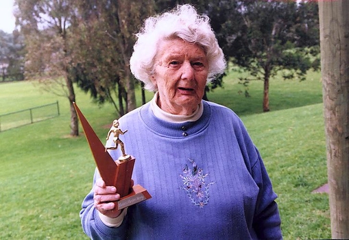 Older woman holds wooden trophy with female runner