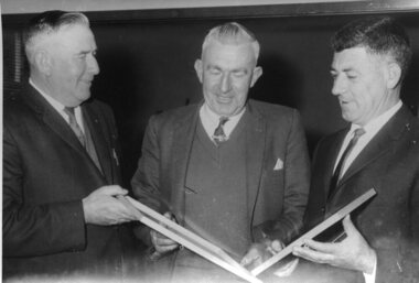 Three men hold two framed certificates